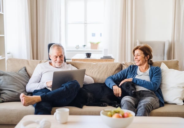 This image of a man and woman using a computer with their dog demonstrates how easy online booking is with Gingr’s dog daycare software.