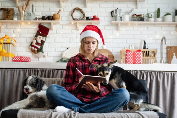 woman with dogs writing list with holiday decor in background