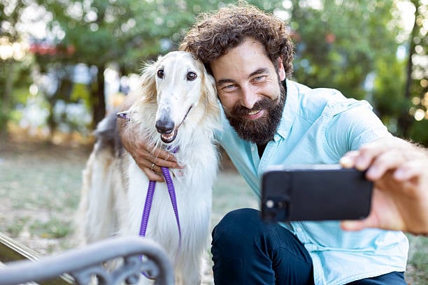 man taking smartphone selfie outside with dog
